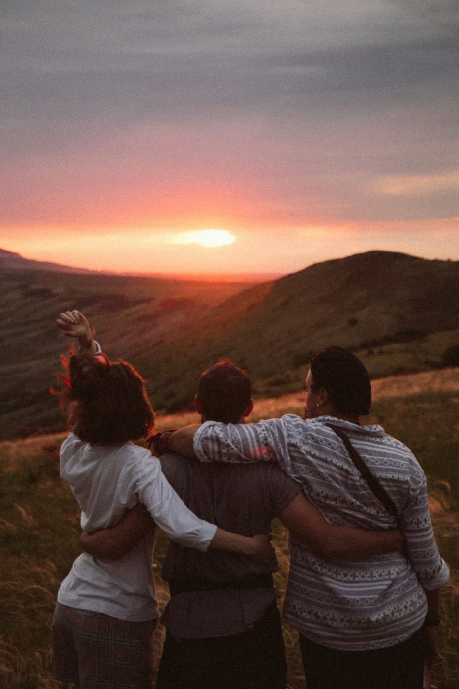 Tres personas abrazadas mirando el atardecer